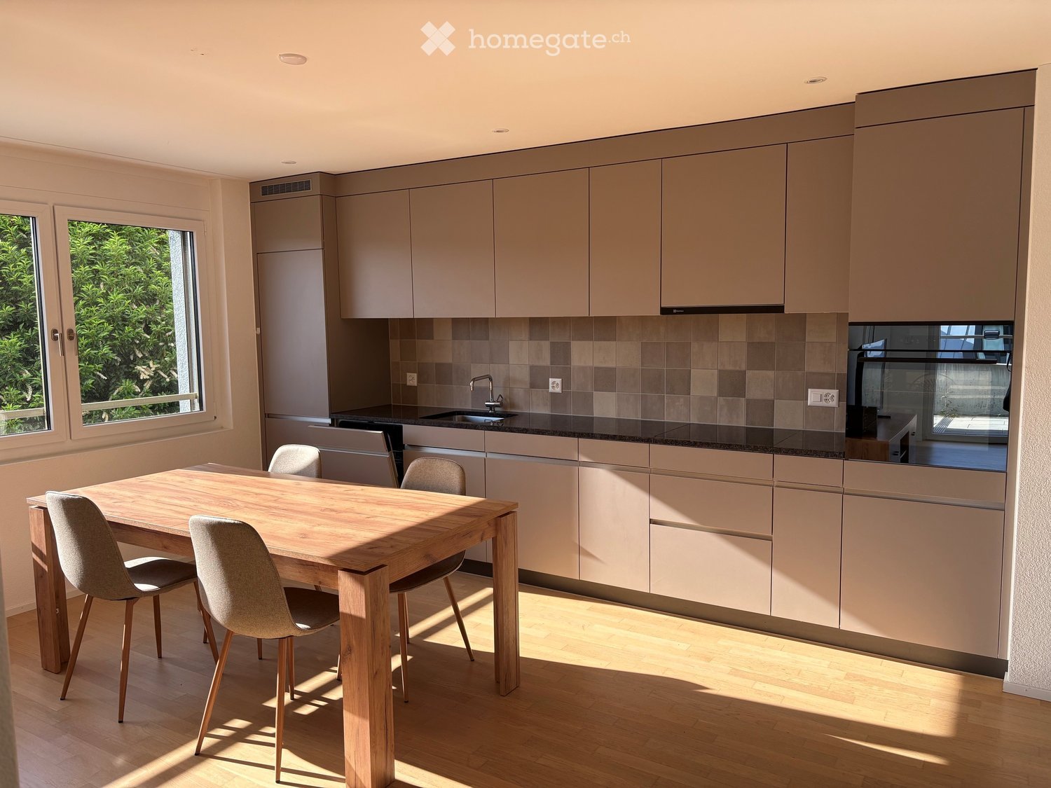 Modern kitchen with light-colored cabinets, a wooden dining table with four chairs, and a sink area with a faucet.