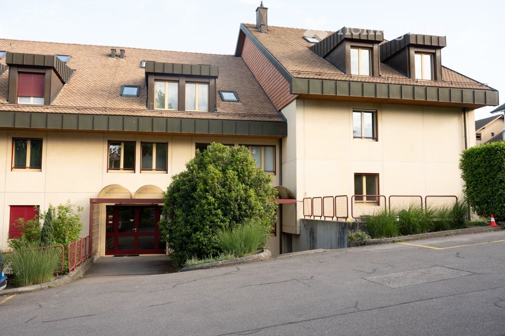Two-story residential building with beige facade, multiple windows, and a central entrance with red double doors.