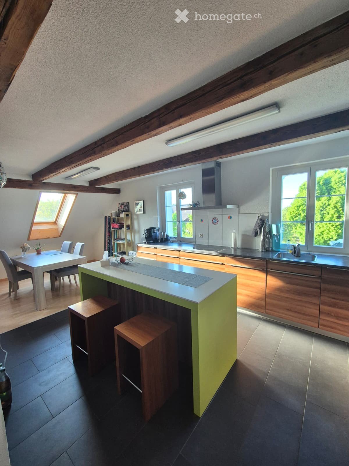 Modern kitchen with exposed wooden beams, a central island, and ample natural light from large windows. Includes a dining area with a table and chairs, and various kitchen appliances.