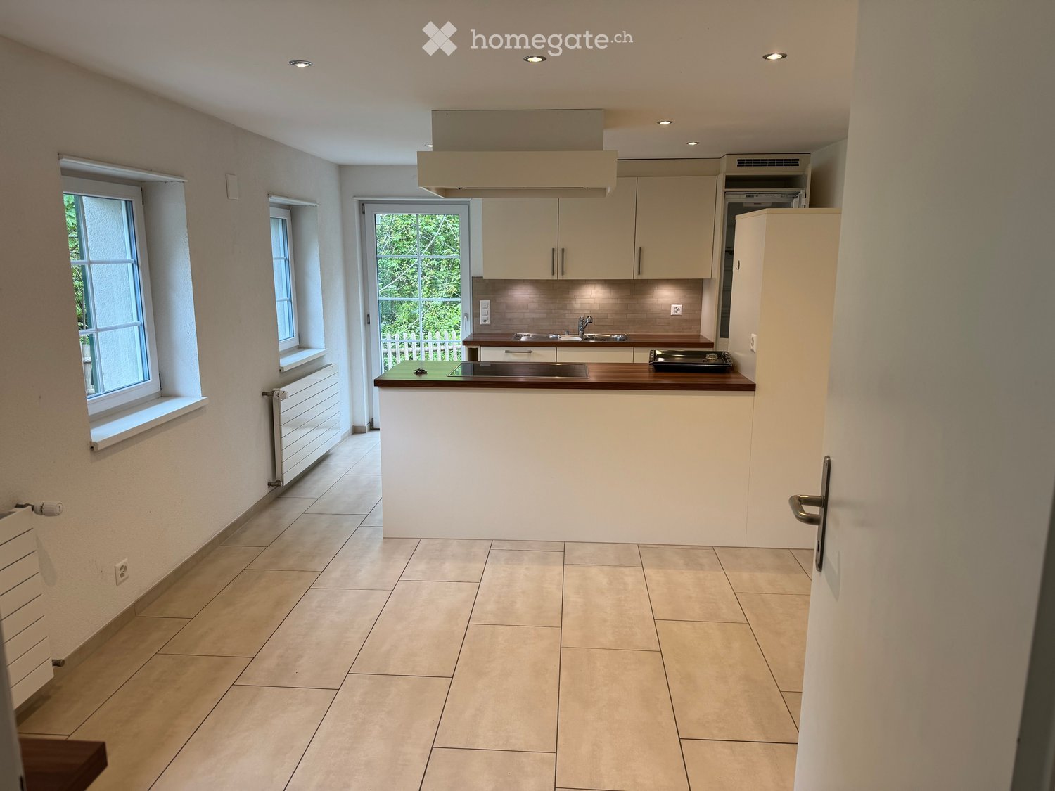 Modern kitchen with light-colored cabinets, a central island, and a tiled floor. Features include a sink, faucet, and stove.
