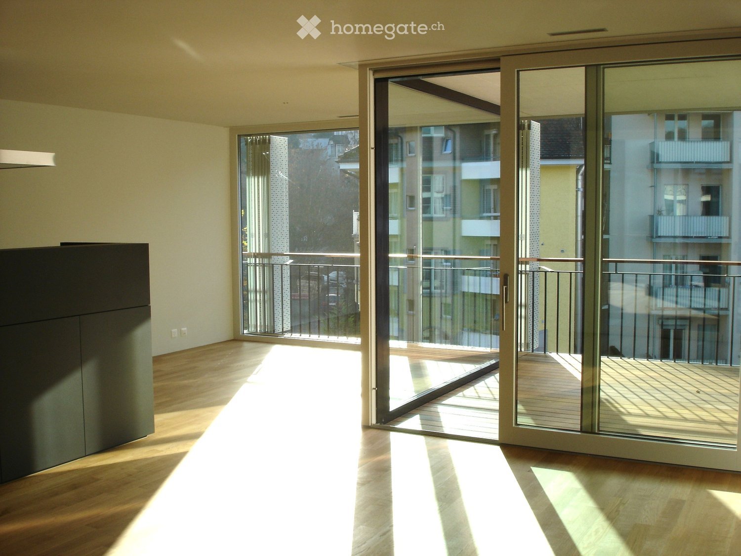 Empty room with wooden flooring, large sliding glass doors leading to a balcony, and natural light streaming in.