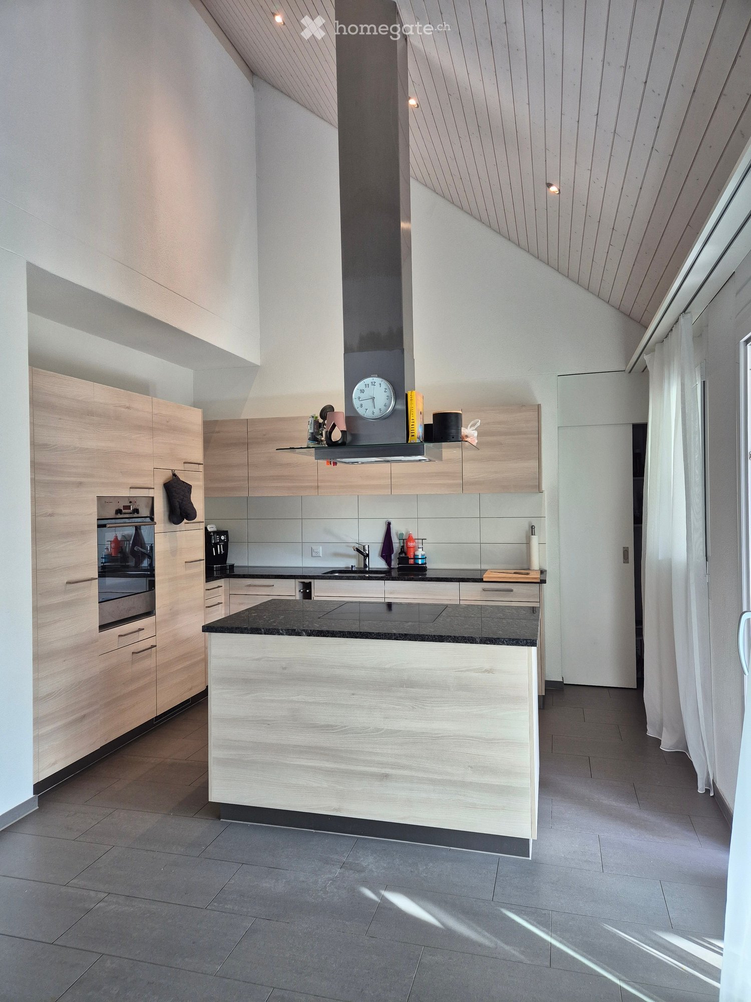 Modern kitchen with light wood cabinets, stainless steel appliances, and a central island with a black countertop.