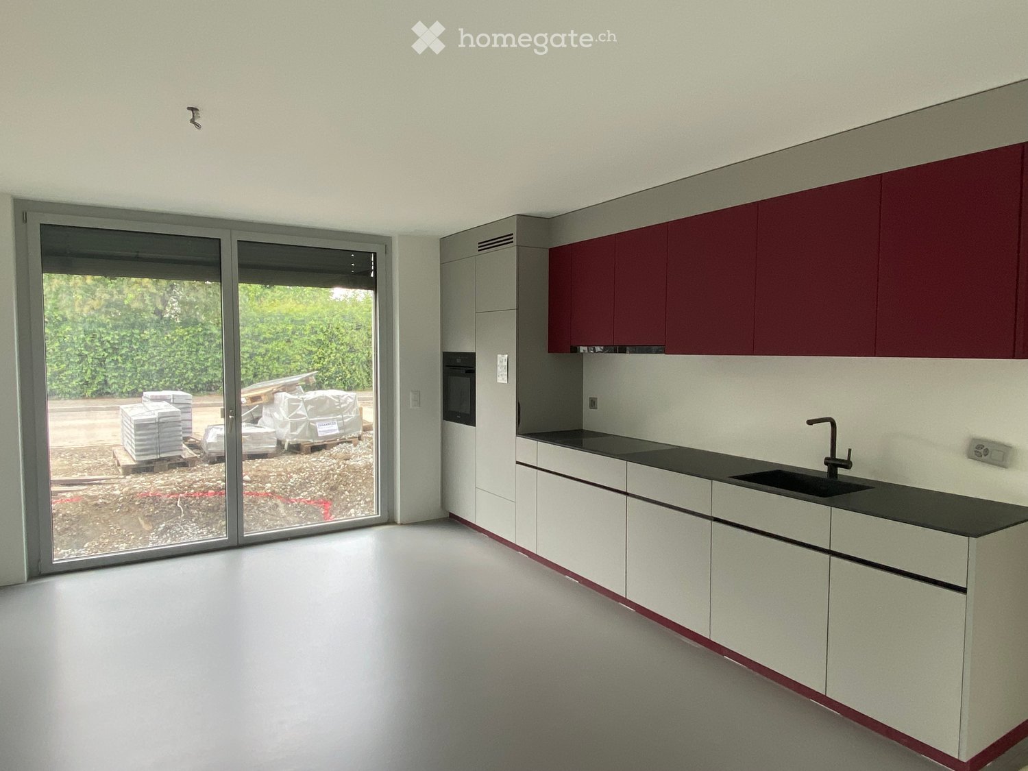 Unfurnished Room. Empty kitchen with white and red cabinets, black countertop, sink, and a large sliding glass door leading to an outdoor area.