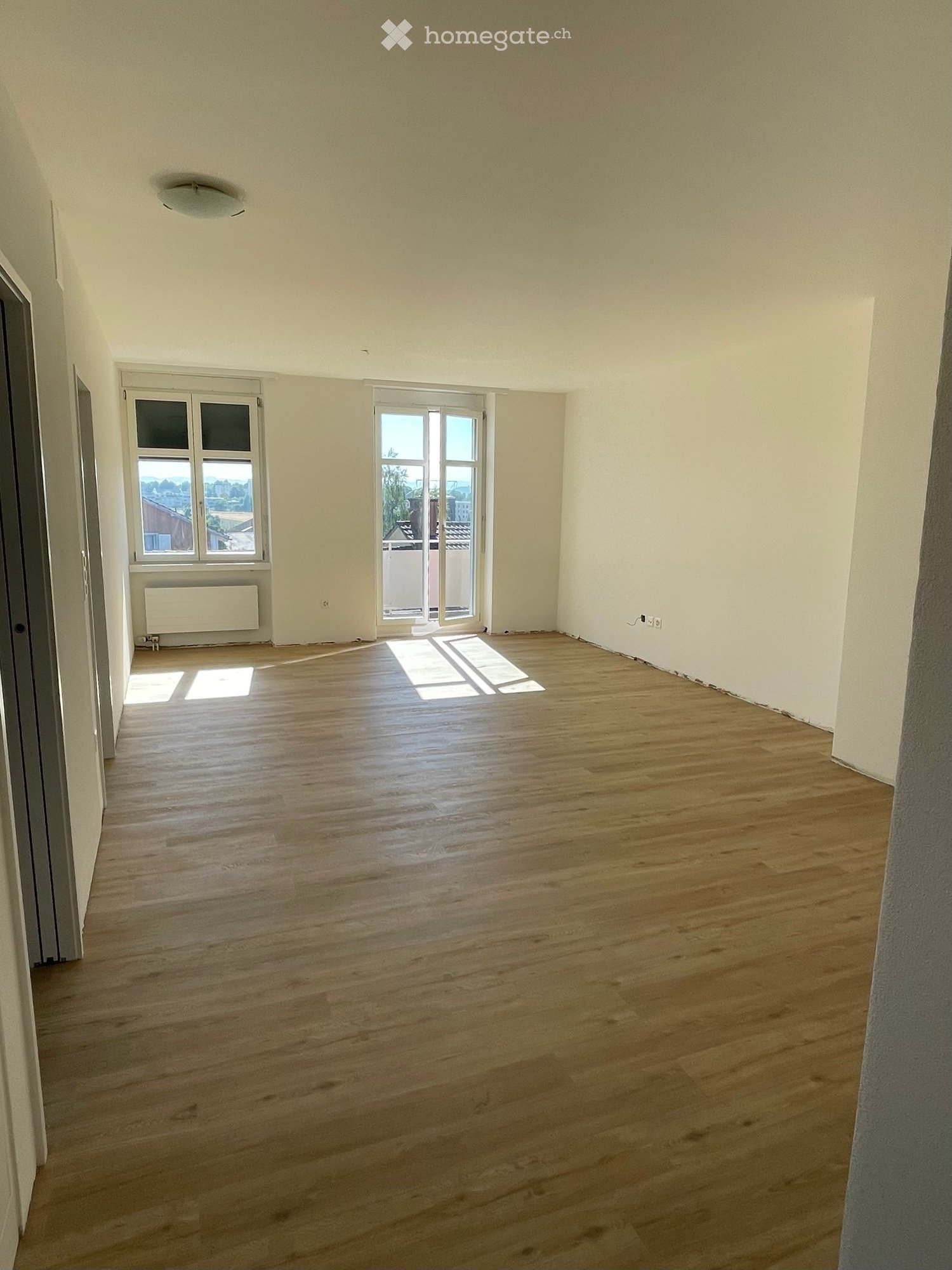 Empty room with wooden flooring, white walls, and large windows allowing natural light. No furniture or equipment is present.