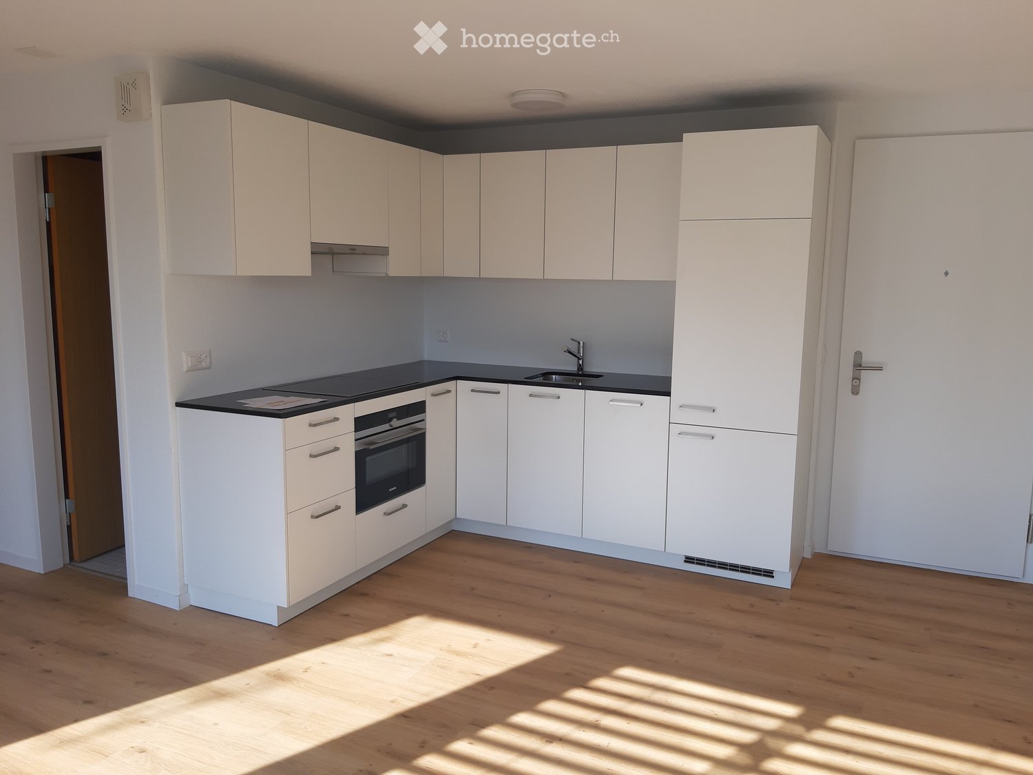 Modern kitchen with white cabinets, black countertops, and wooden flooring. Features include an oven, sink, and faucet.