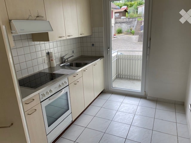 Modern kitchen with white cabinets, tiled walls, and a built-in oven and stove. A sliding glass door leads to a small balcony.