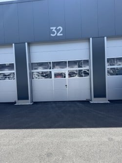 A modern industrial-style building with large garage doors, featuring the number "32" displayed above the central entrance.