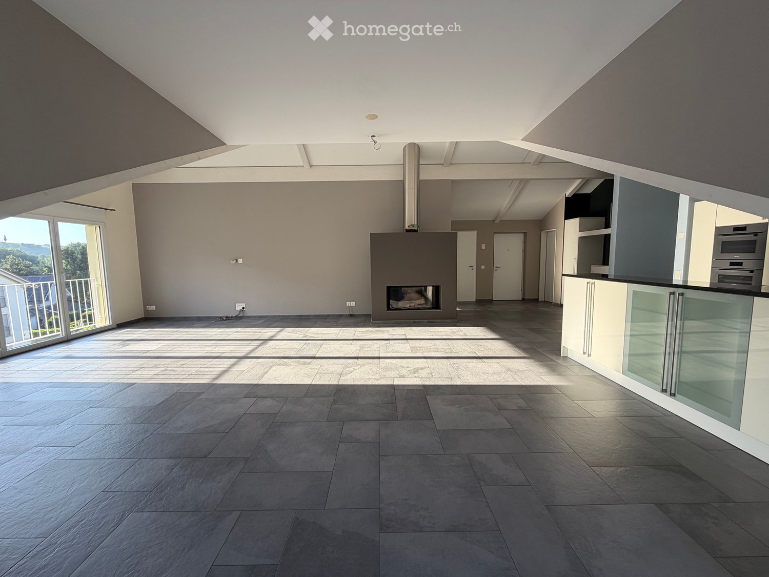 Open-plan living and dining area with a modern fireplace, large windows, and a kitchen area with cabinets and an oven.