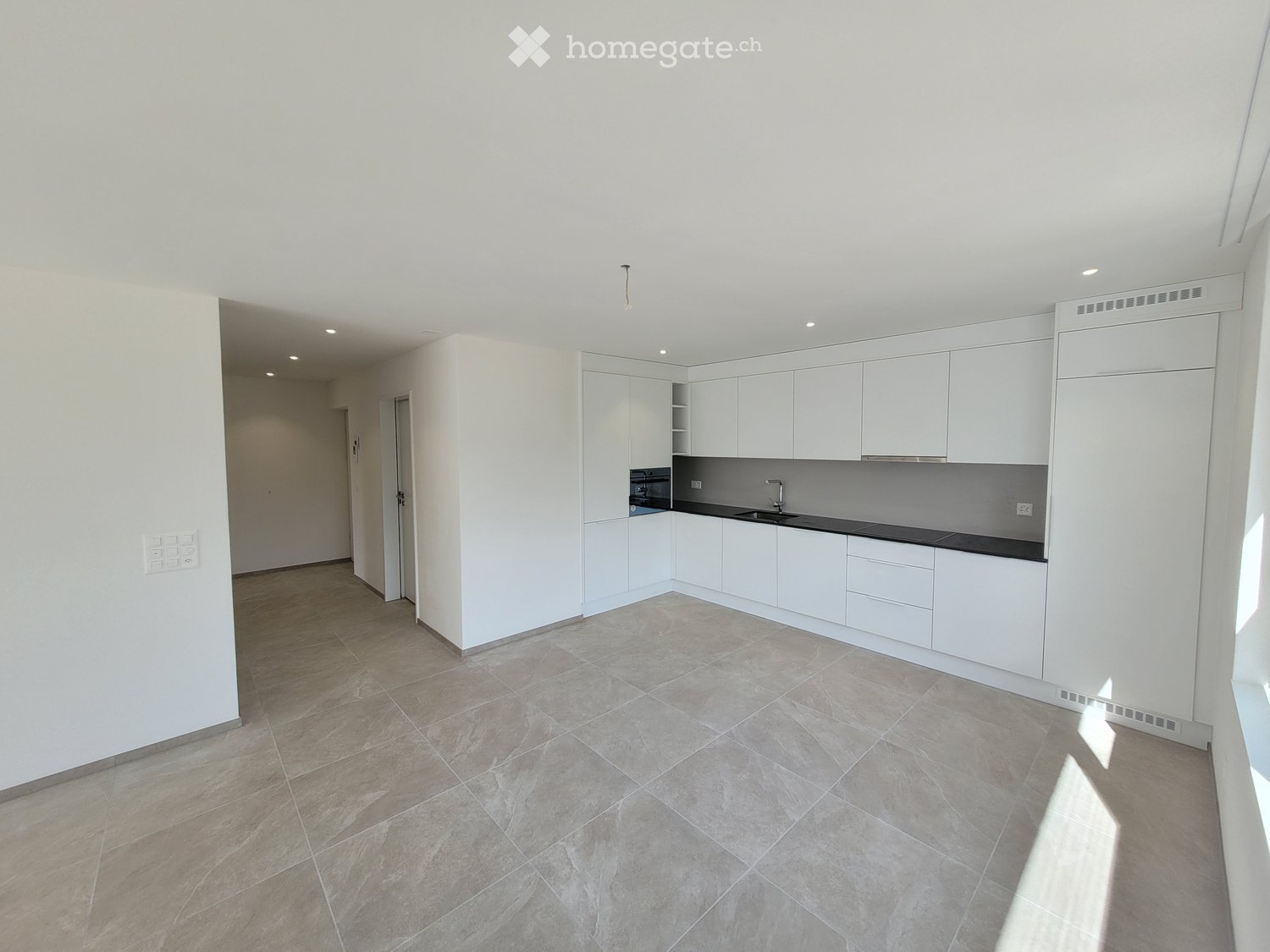 Empty kitchen with white cabinets, dark countertops, and tiled floor. No appliances or furniture present.