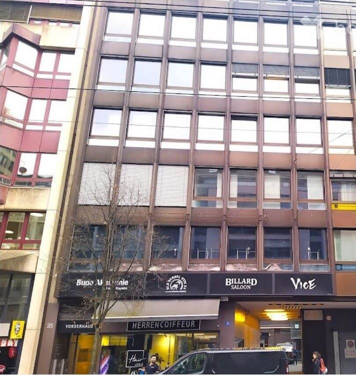 Multi-story building with commercial storefronts including "Billiard Saloon" and "Herren-Coffeur" on the ground floor, with large windows and signage.