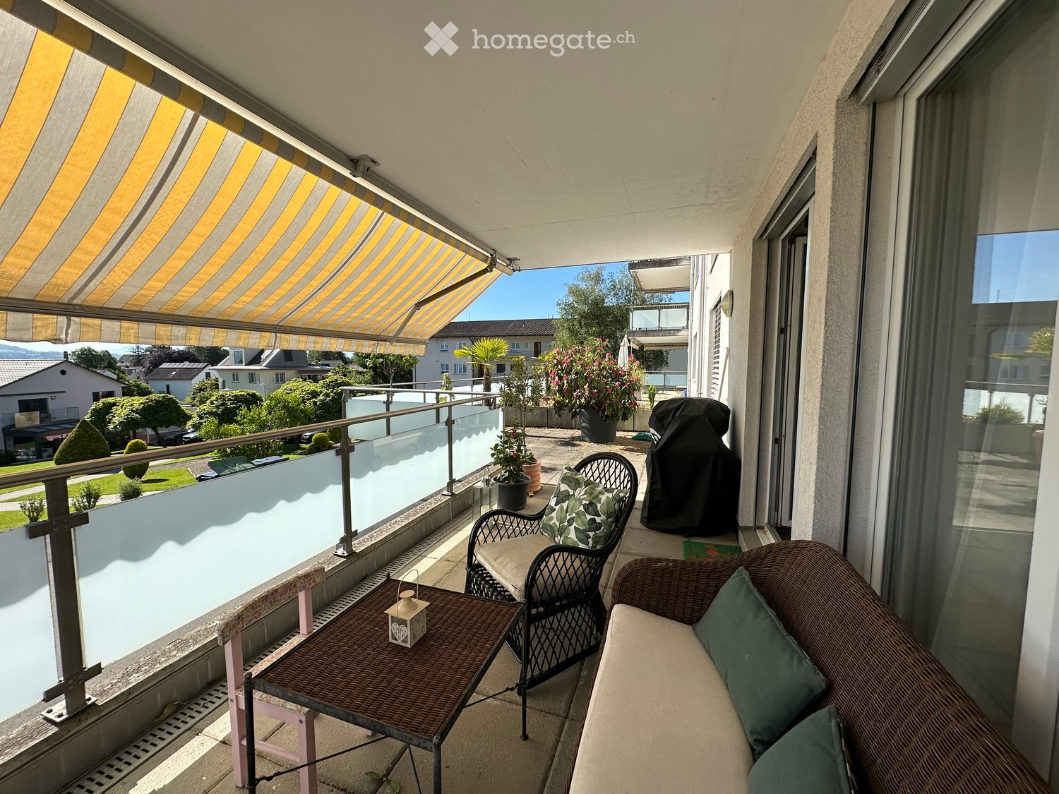 Balcony with a sofa, table, and chairs, featuring a striped awning and a view of the neighborhood.