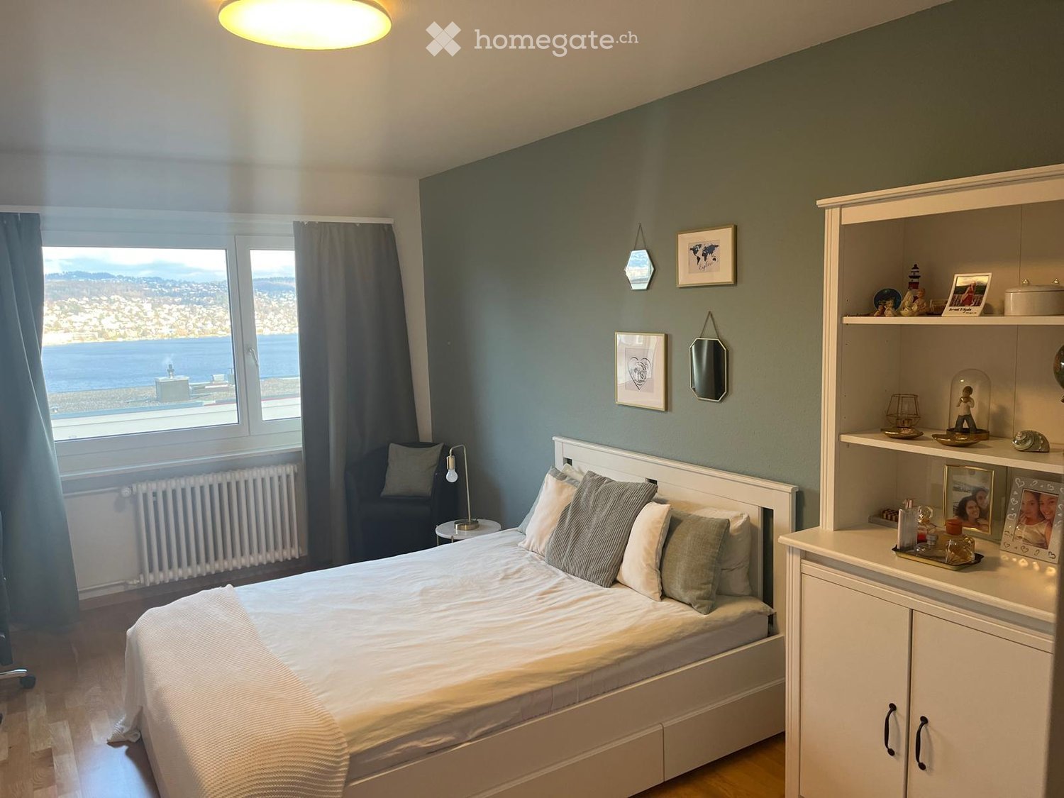 Cozy bedroom with a large bed, nightstand, lamp, chair, and cabinet. Offers a scenic view through large windows.