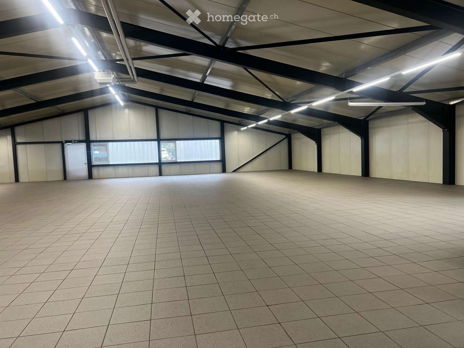 spacious room, tiled floor, fluorescent ceiling lights, white walls, steel framework, door on the left