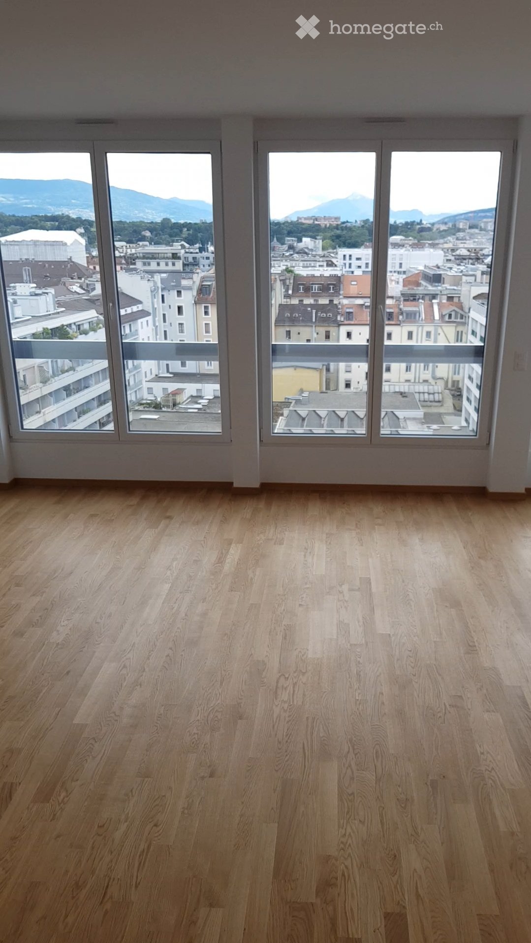 Empty room with wooden flooring and large windows offering a cityscape view.