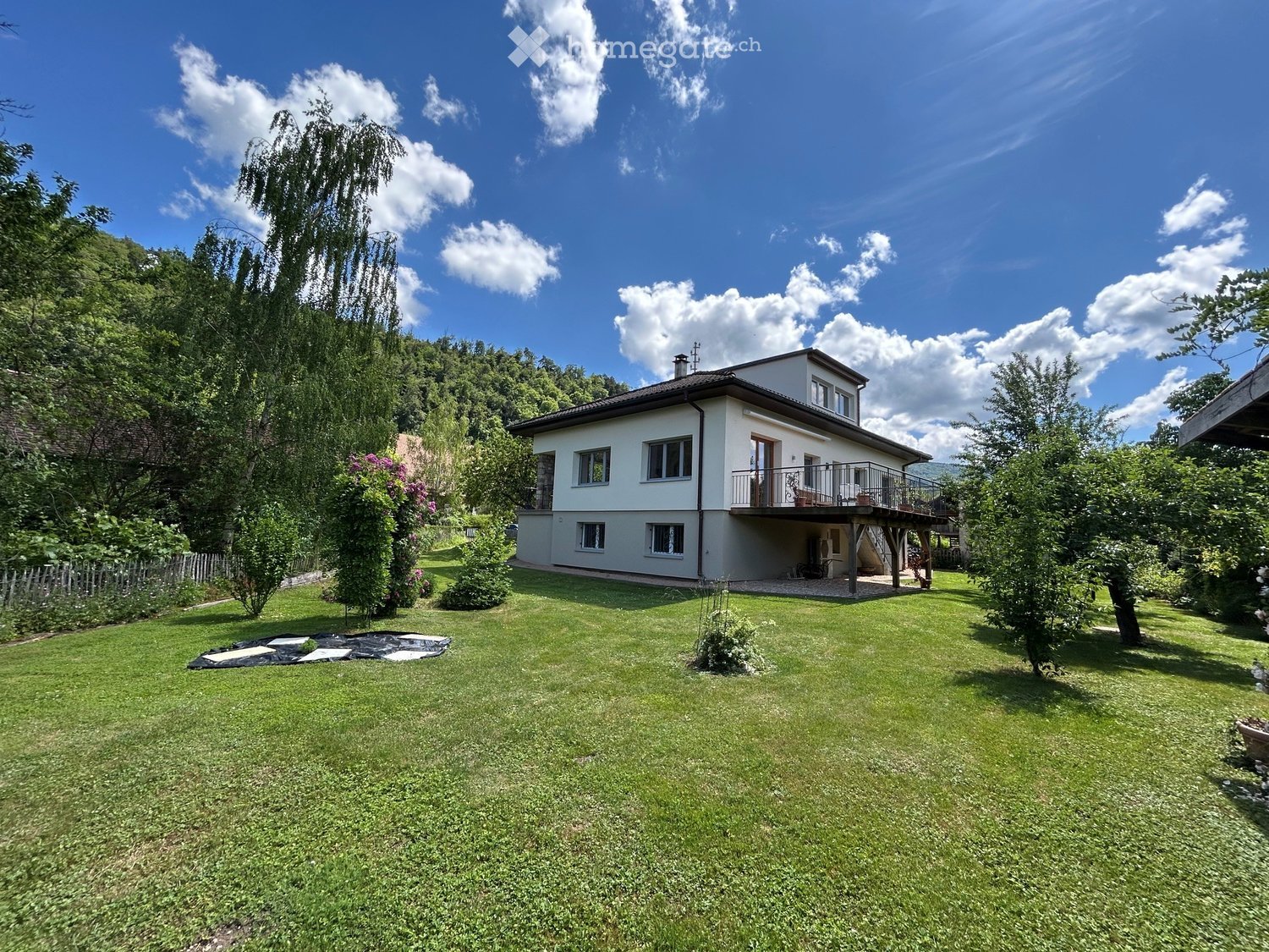 Two-story house with a balcony, surrounded by a well-maintained lawn and trees.