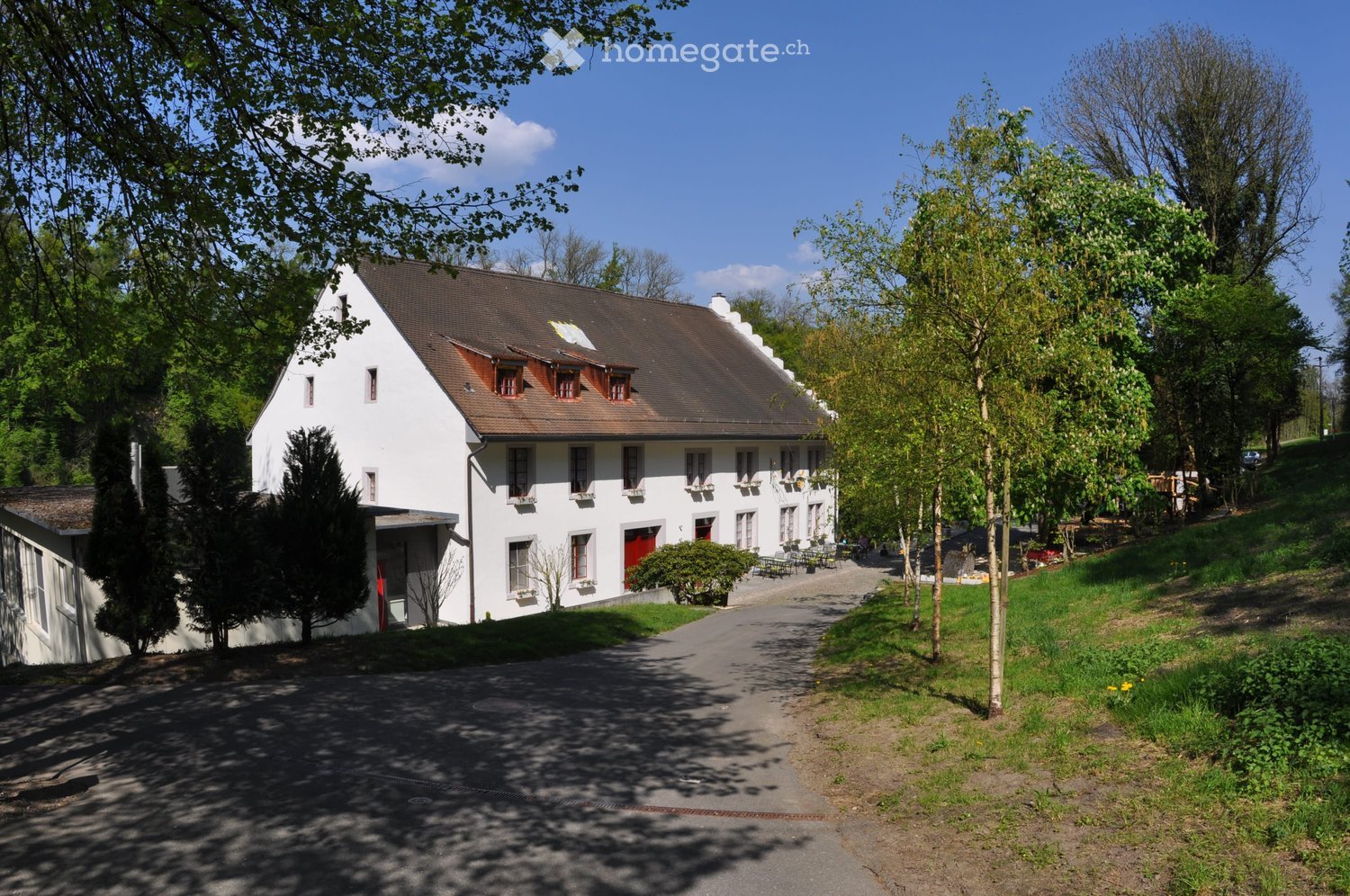 Raised ground floor, white exterior, multiple windows, red front door, gray roof