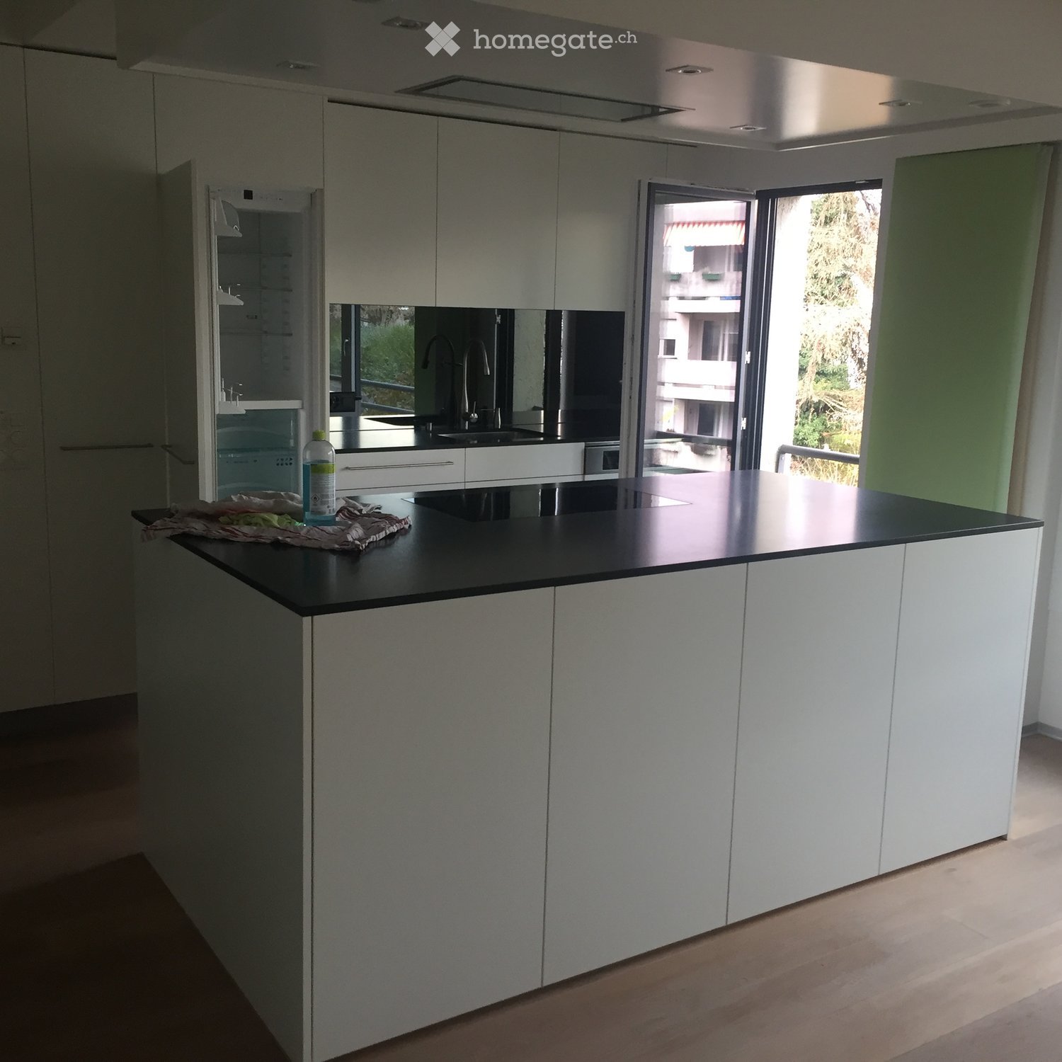 Modern kitchen with white cabinets, black countertop, and a sink area. A bottle is placed on the counter, and a cleaning cloth is visible.