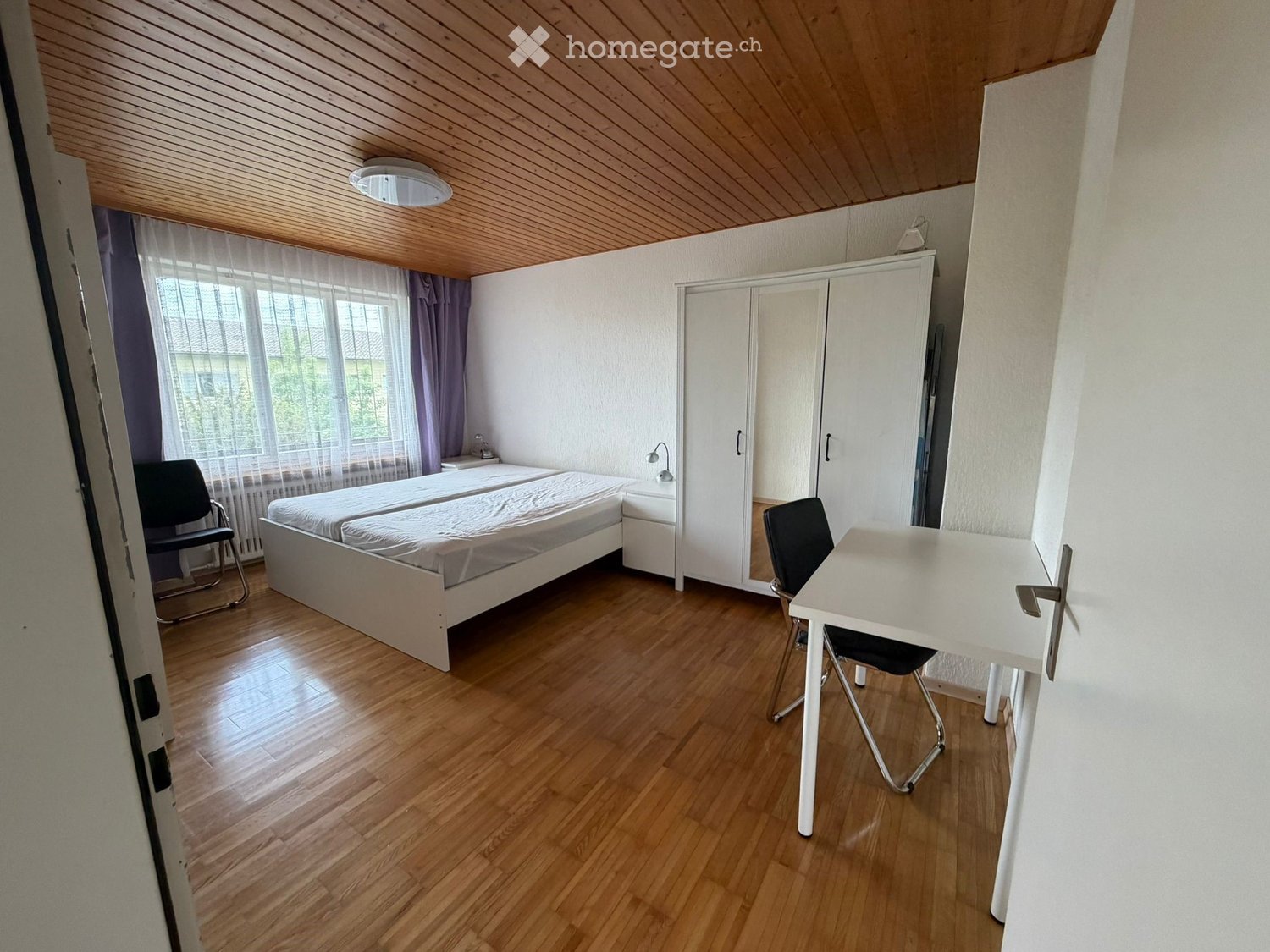 Bright bedroom with wooden flooring, a single bed, a desk with a chair, a wardrobe, and a nightstand.