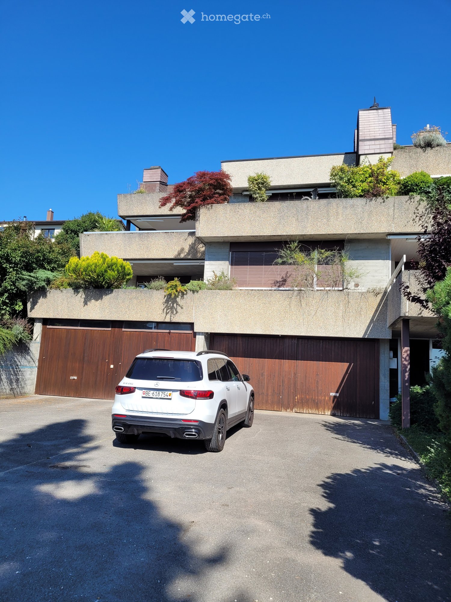 Modern two-story house with a flat roof, large wooden garage doors, and a white SUV parked in front.