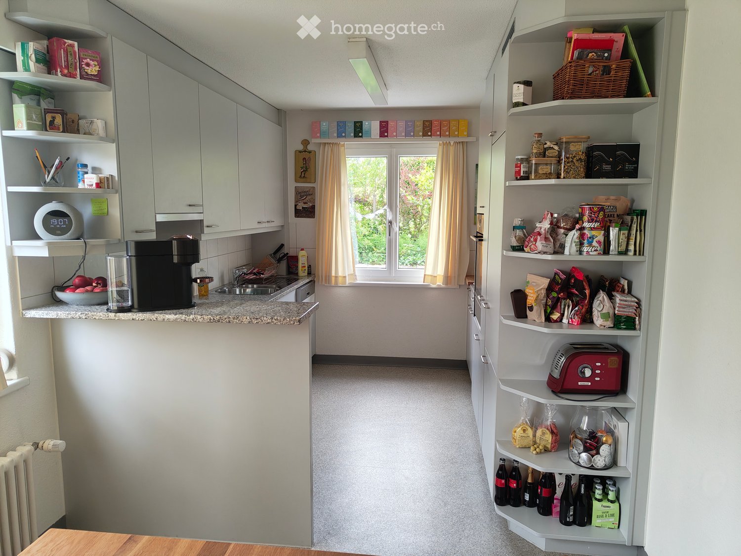 Modern kitchen with white cabinets, granite countertop, and built-in shelving. Features a coffee maker, sink, and various food items on shelves.