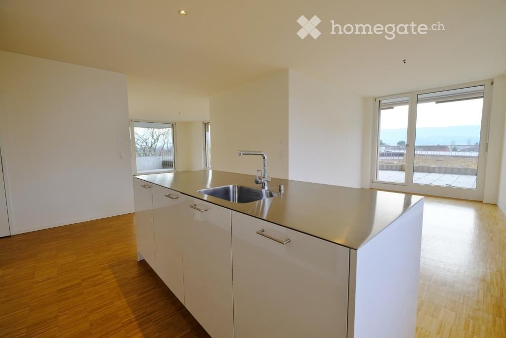 Modern kitchen with white cabinets, stainless steel sink, and wooden flooring. Large windows provide natural light and a view.
