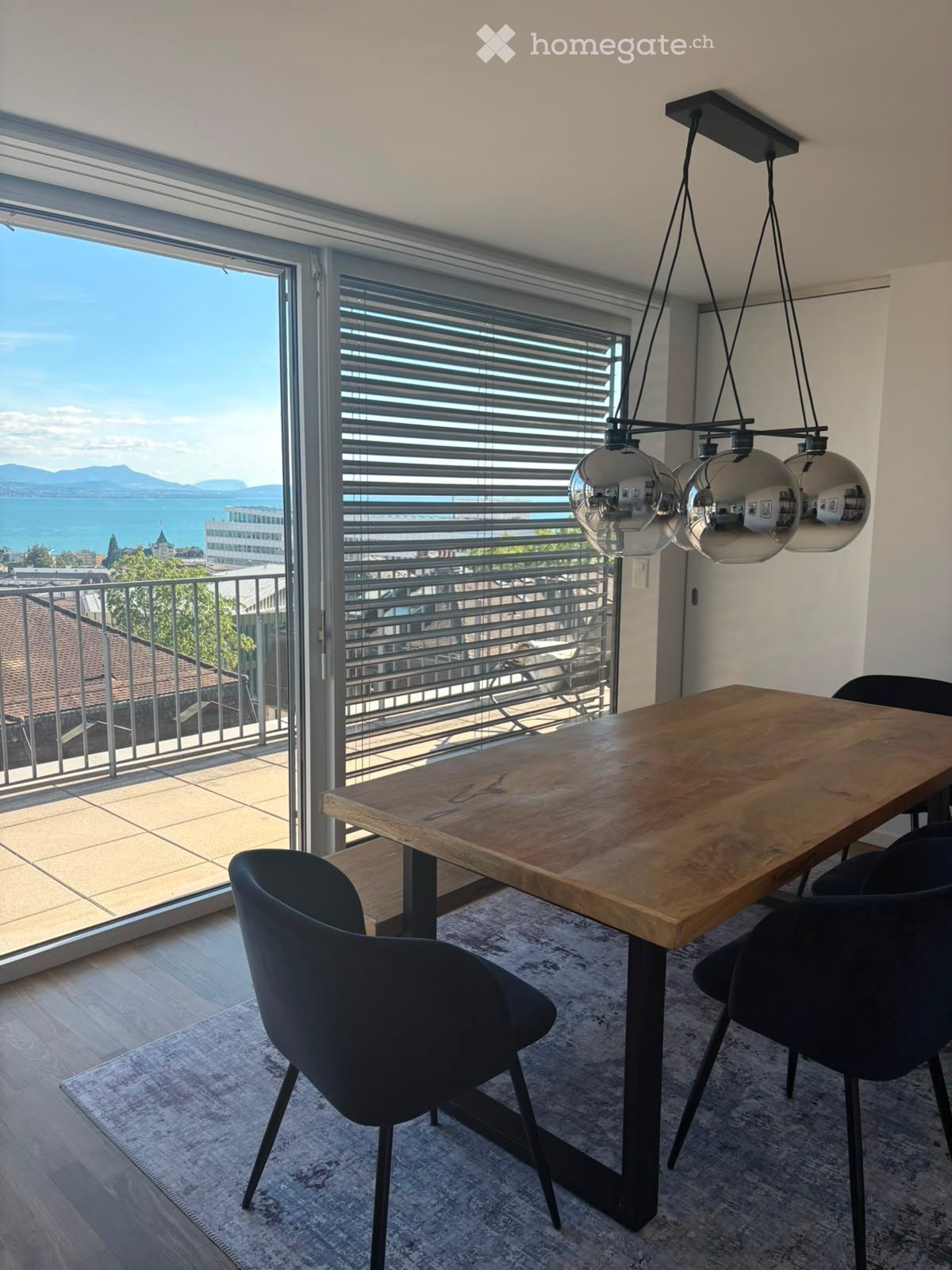 Modern dining area with a wooden table, black chairs, pendant lights, and large windows offering a scenic view.