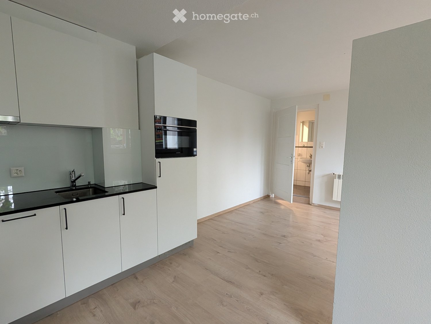 Modern kitchen with white cabinets, black countertop, and a sink. A microwave is mounted above the countertop, and the floor is wooden.