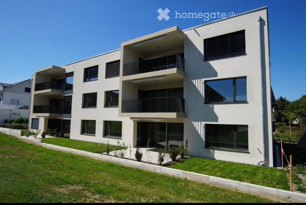 Modern, three-story apartment building with white facade, large windows, and multiple balconies.