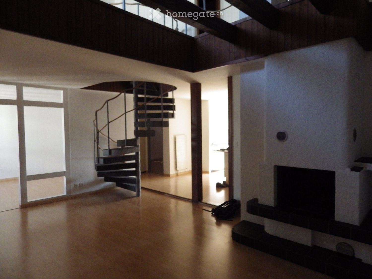 Open-plan living space with wooden flooring, large windows, a modern spiral staircase, and a fireplace area.