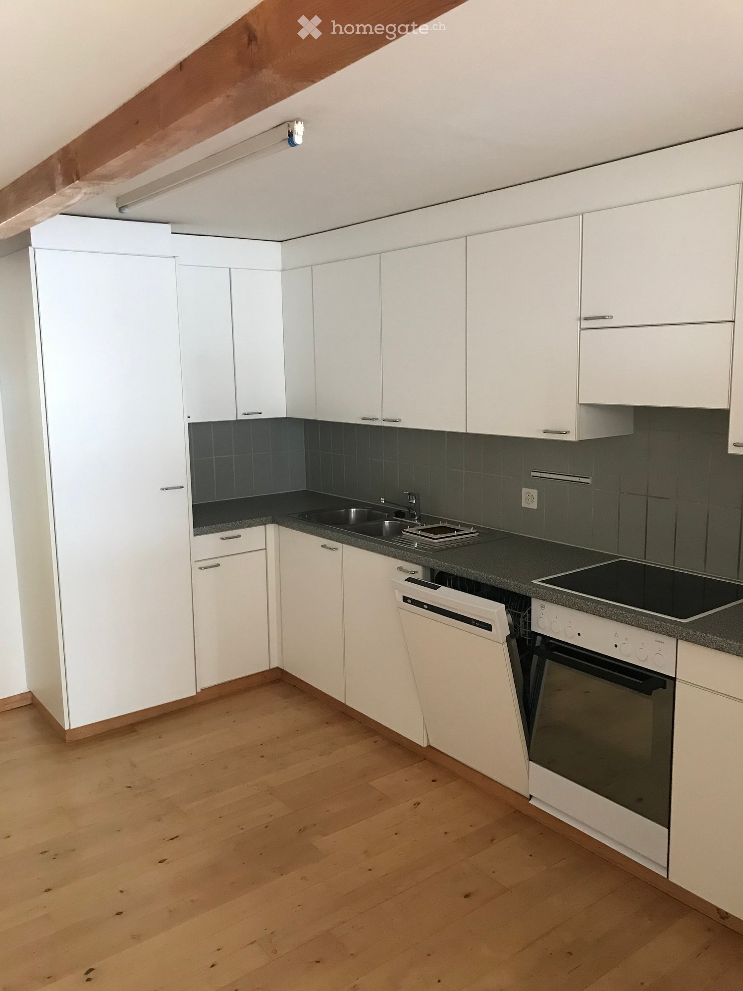 Modern kitchen with white cabinets, dark countertops, and stainless steel appliances including a sink, dishwasher, and oven. The floor is light wooden.