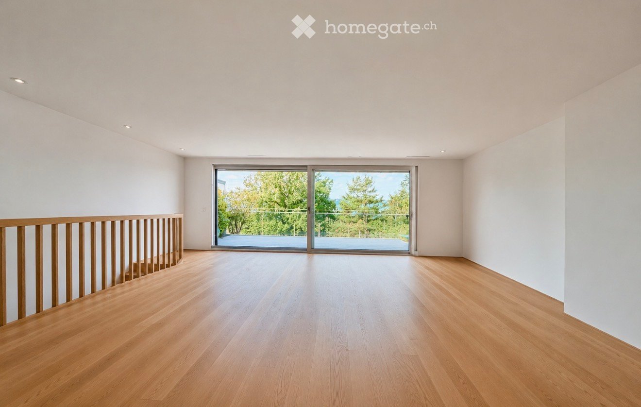 Bright, empty room with wooden flooring, white walls, and large sliding glass doors leading to a balcony with a view of trees.