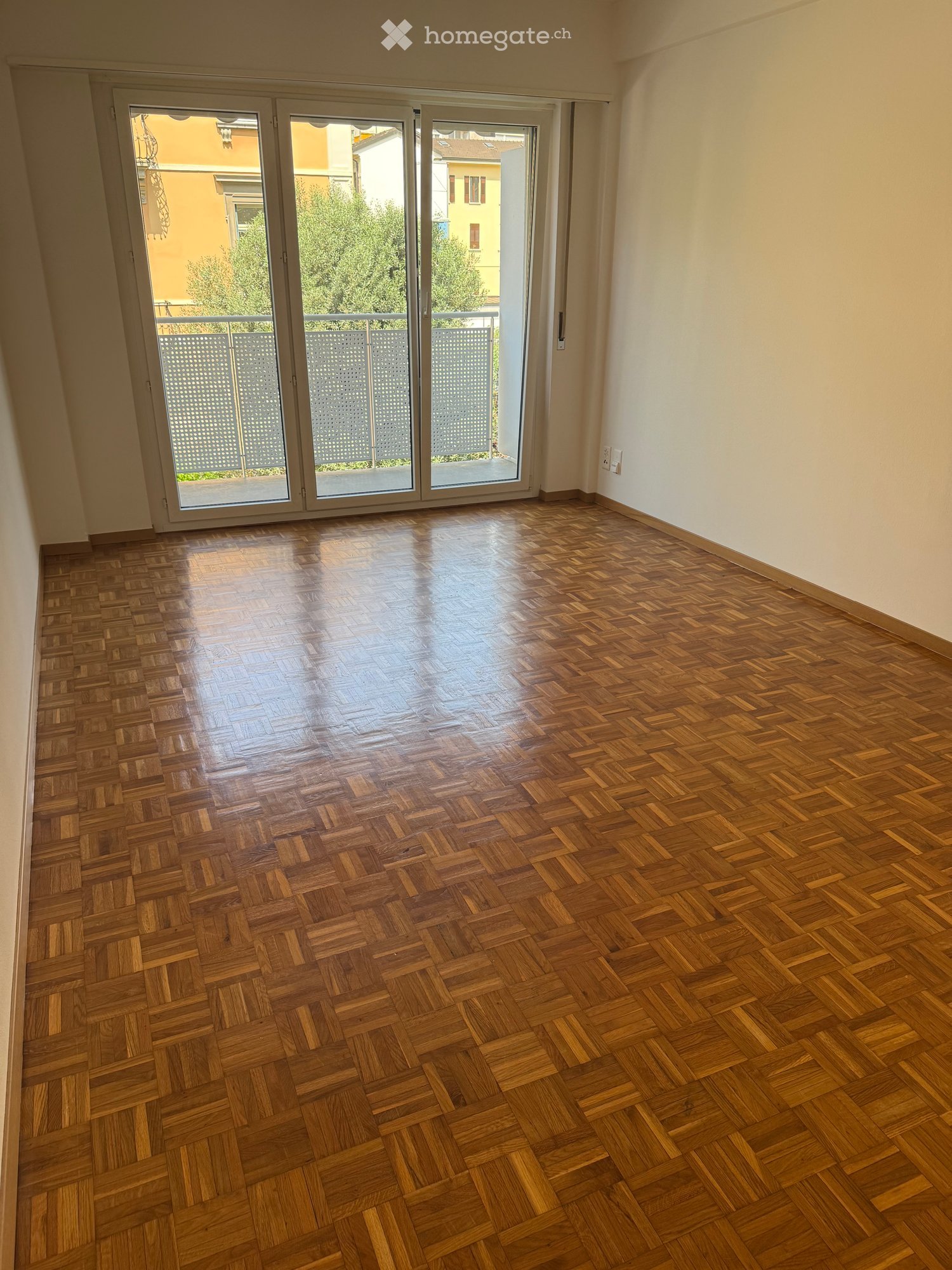 Empty room with polished wooden parquet flooring and large sliding glass doors leading to a balcony or outdoor area.