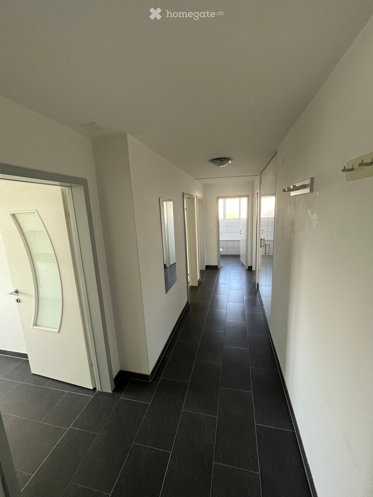 Clean, narrow hallway with dark tiled flooring, white walls, and several doors leading to different rooms.