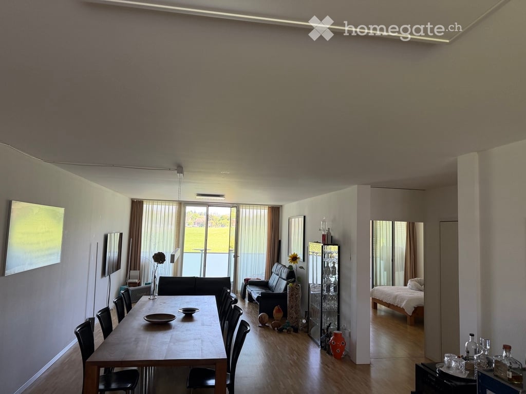 Open-plan living and dining area with modern furniture, large windows, and a view of the outdoor space.