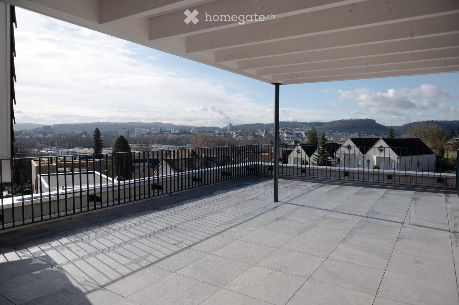 Balcony with tiled floor, metal railing, and a view of the city and surrounding landscape.