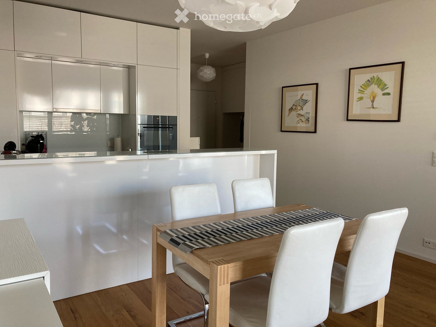 White cabinetry, white countertops, black table, four white chairs, two picture frames, black appliance