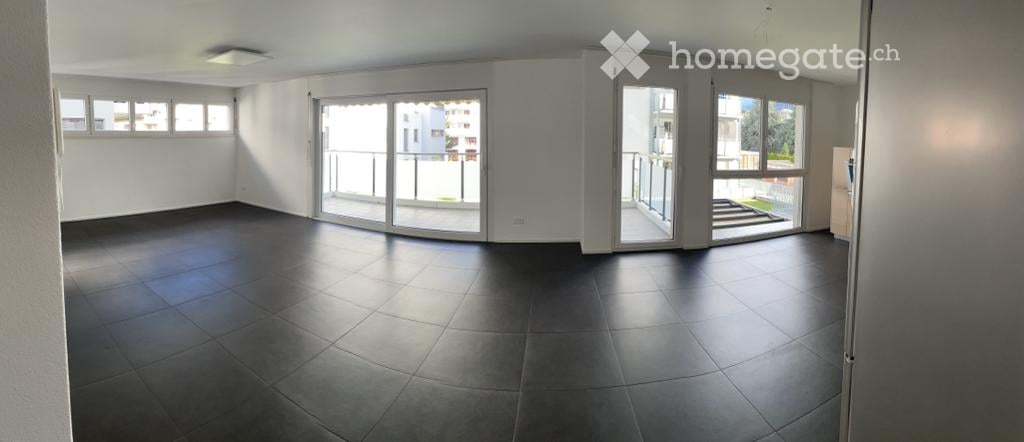 Empty room with dark tiled floor, white walls, large sliding glass doors leading to a balcony, and several windows allowing natural light.