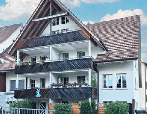 A multi-story residential building with a traditional pitched roof, balconies, and decorative flower boxes.