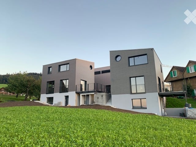 Modern two-story house with grey and beige exterior, large windows, and balconies.