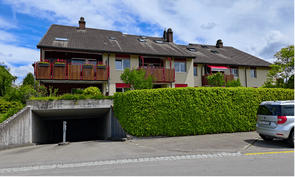 Multi-story residential building with balconies, garage entrance, and neatly trimmed hedge in front.