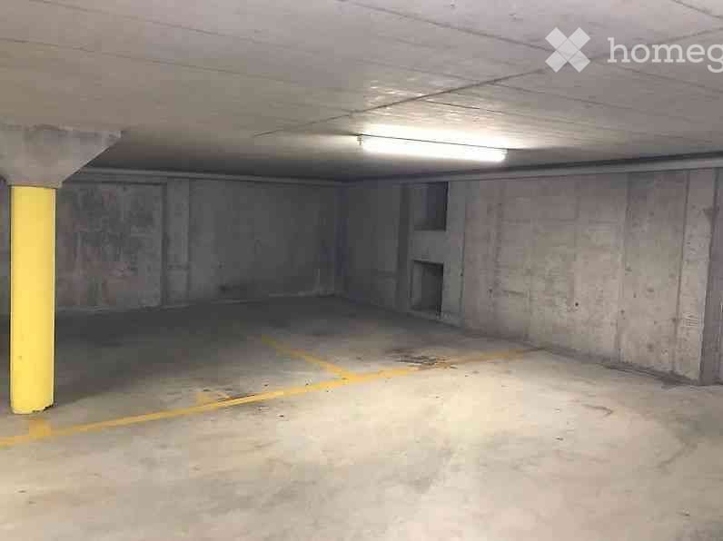Empty underground parking space with concrete walls, a single yellow support column, and a marked parking area.