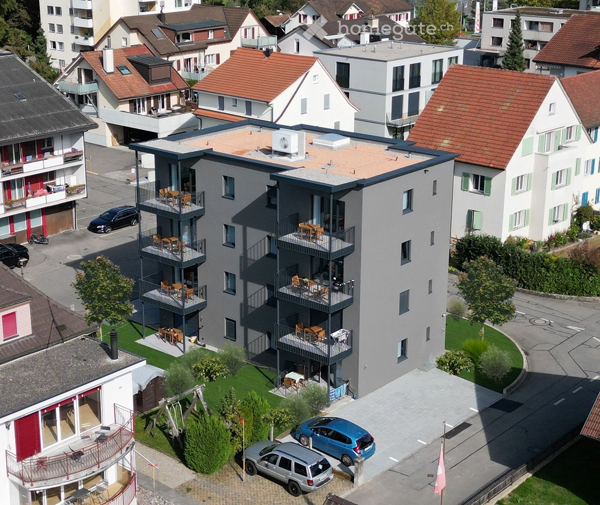 4-story apartment building, balconies on multiple floors, green lawn, multiple parked cars