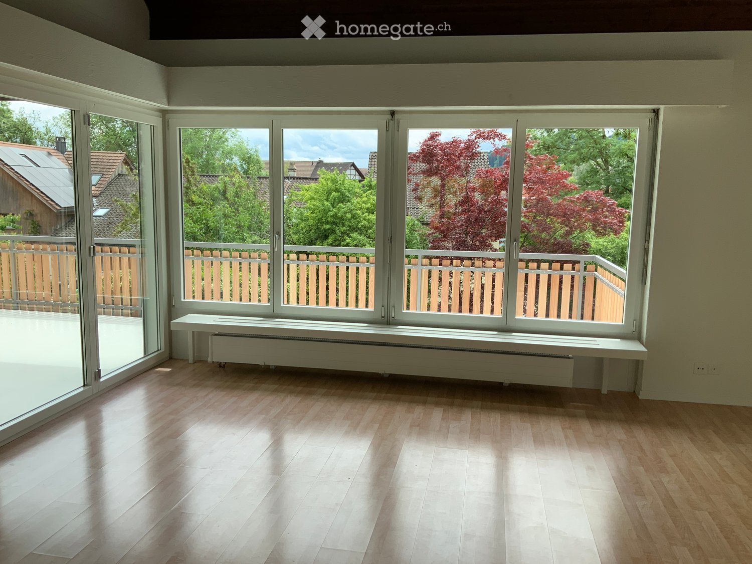 Empty room with wooden flooring, large windows, and a radiator under the windows.