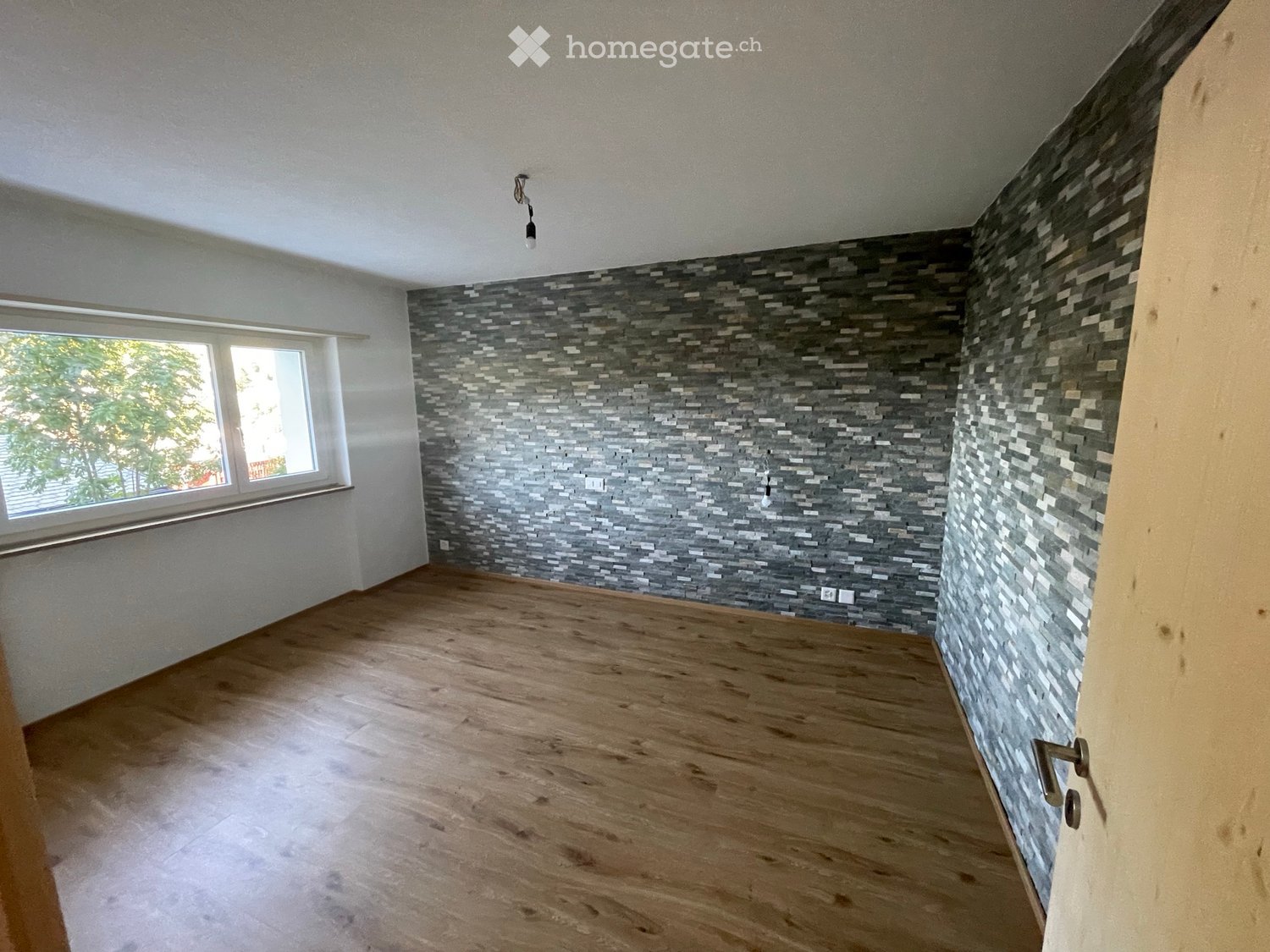 Empty room with wooden flooring, large window, and decorative tiled accent wall.