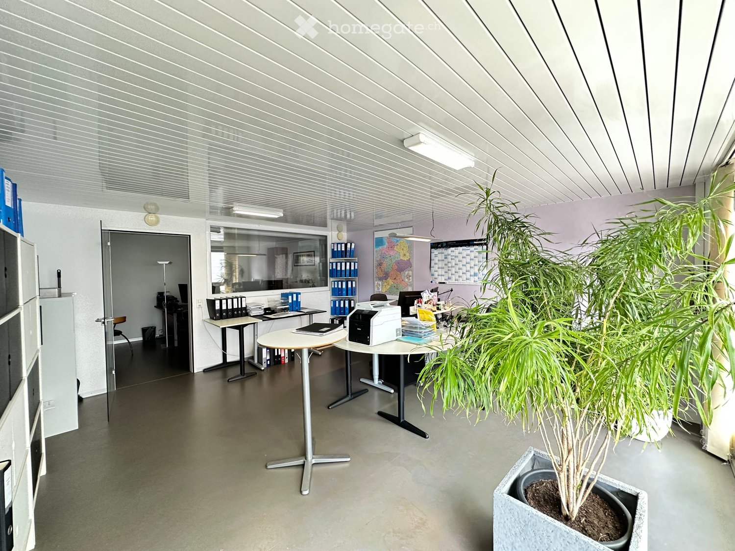Office space with round tables, chairs, printer, filing cabinets, and large potted plants.