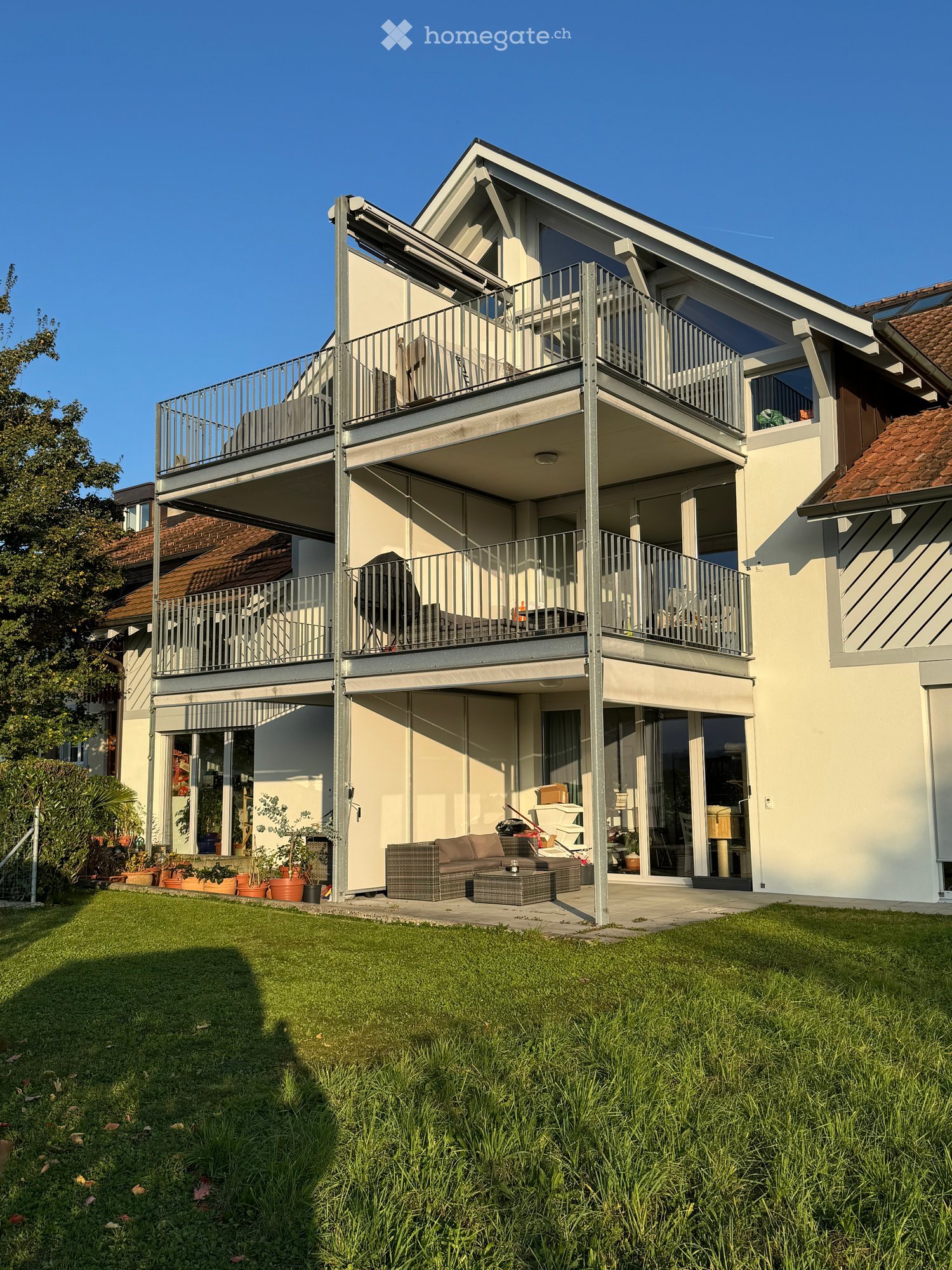 Modern two-story house with balconies, large windows, and a well-maintained garden with seating area.