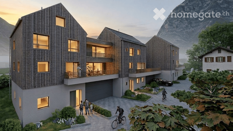 Modern multi-story residential building with wooden facade, large windows, balconies, garage, and parking area, set against a scenic mountain backdrop.