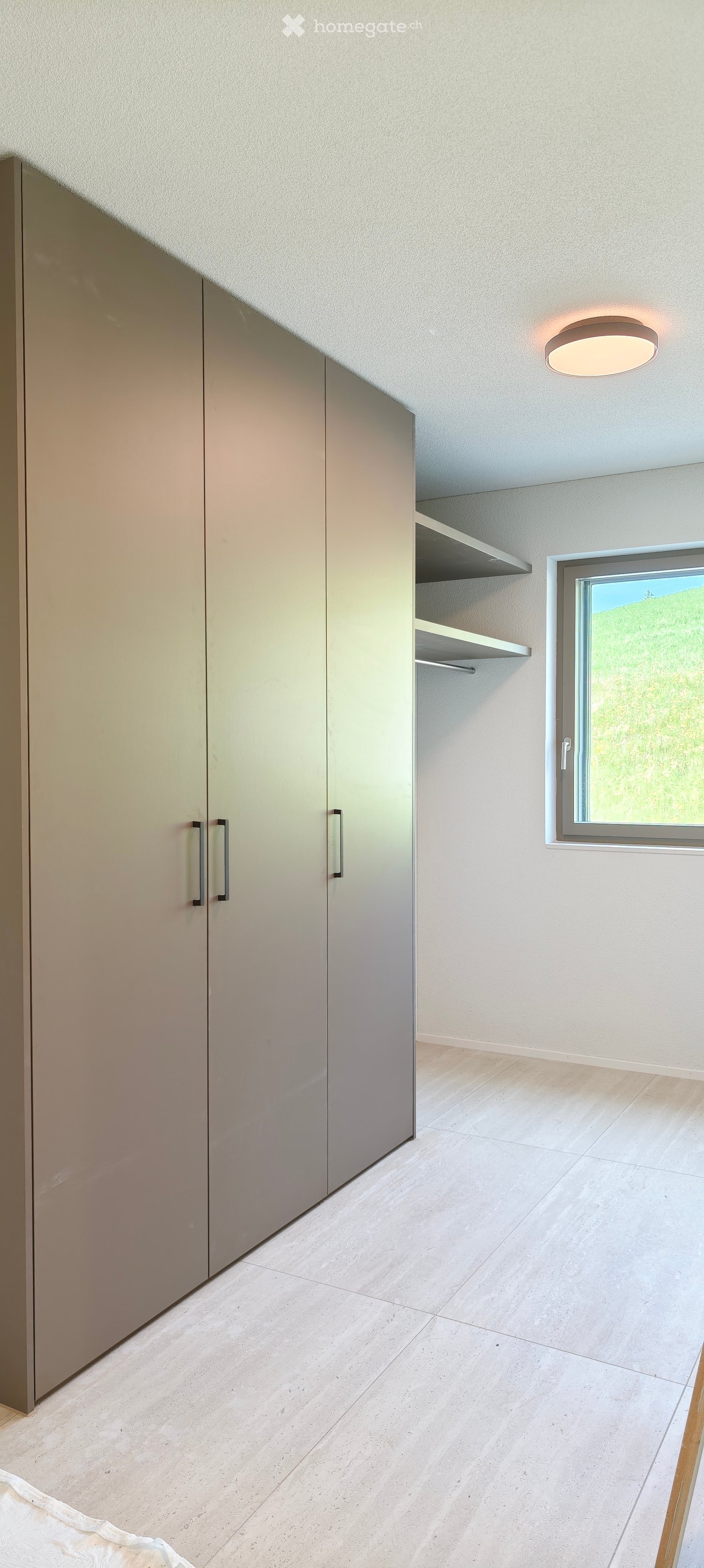 Empty room with light-colored tiled floor, built-in closet with mirrored doors, window with view, and recessed ceiling light.