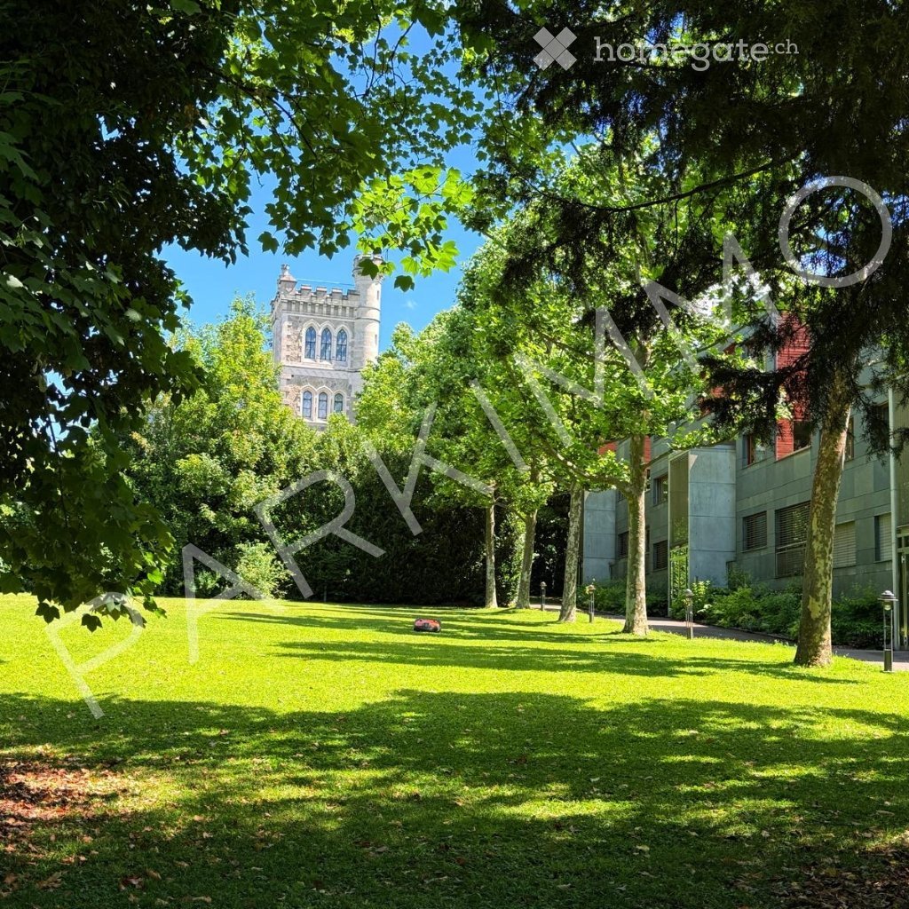 A well-maintained lawn with mature trees, a historic tower in the background, and a modern building to the right.