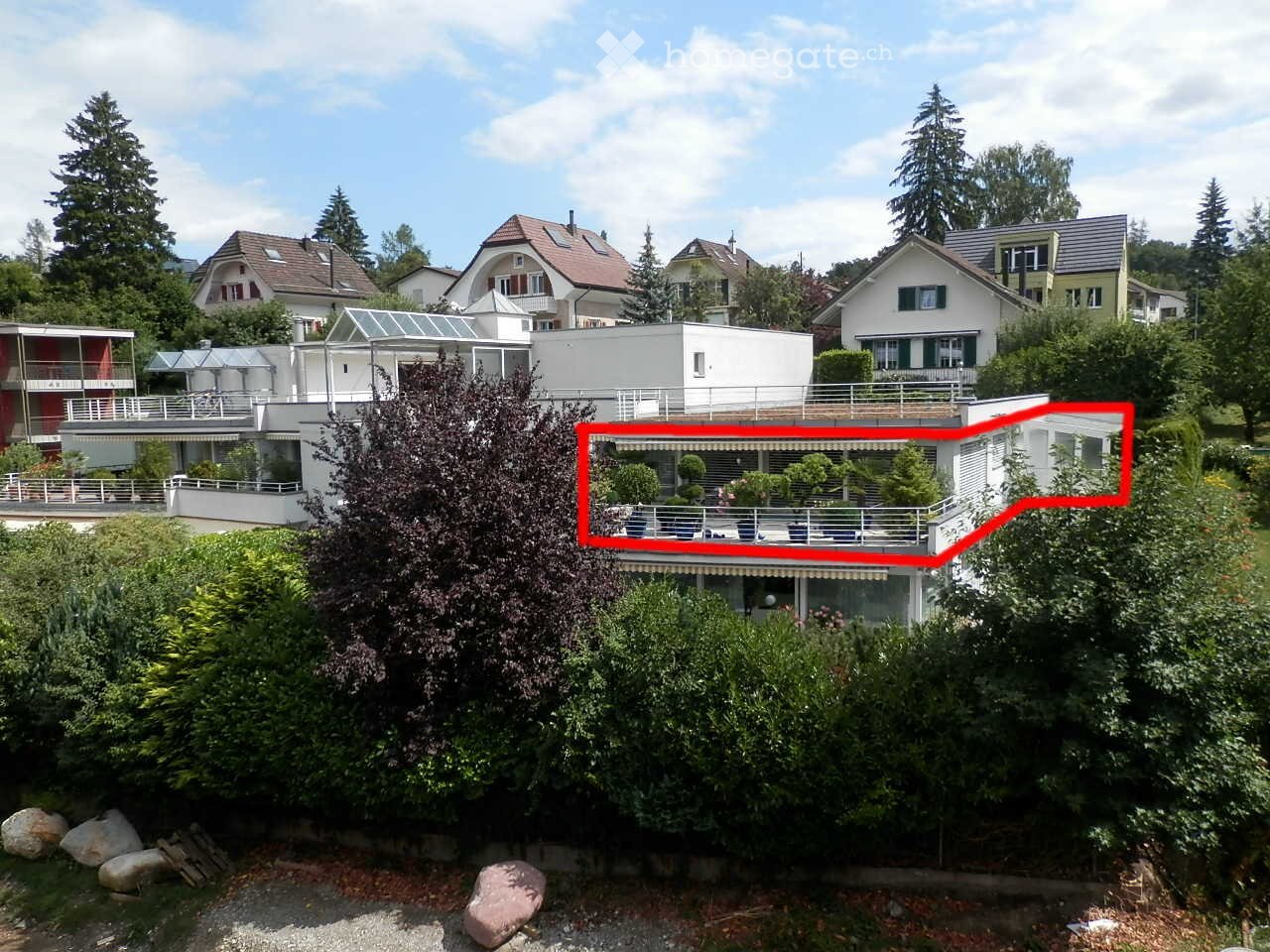 A modern house with a large balcony and surrounding greenery, featuring multiple levels and contemporary design.